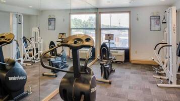 Un gimnasio con diversos equipos de ejercicio, amplias ventanas y vistas al exterior.
