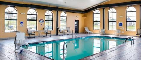 Una amplia piscina interior con numerosas tumbonas y suelo de baldosas.