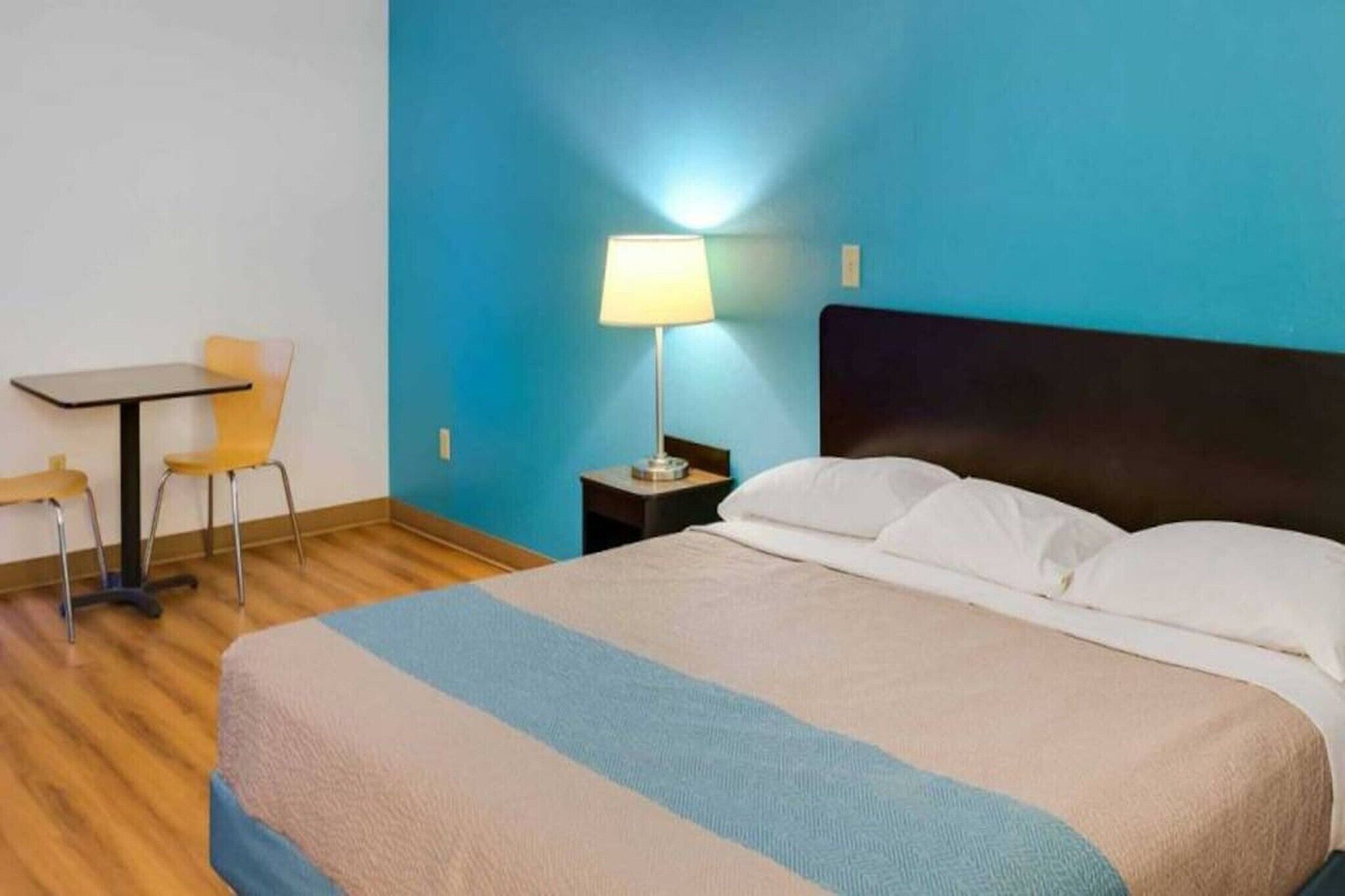 Una habitació d'hotel amb un llit, escriptori, cadira i tauleta de nit amb una làmpada.