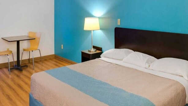 Een hotelkamer met een bed, een bureau, een stoel en een nachtkastje met een lamp.