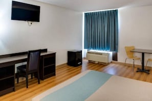 A room with a desk, chair, and a television mounted on the wall.