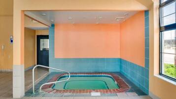 A swimming pool area with a tiled floor, a pool ladder, and a view of the outdoors through a window.