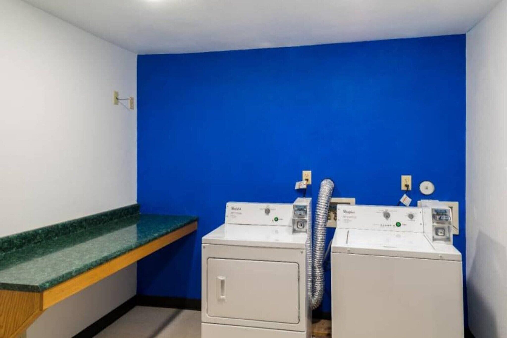 A laundry room with two front-loading washing machines, a green countertop, and a blue wall.