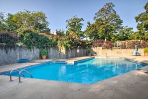 Ein Schwimmbecken mit Betonumrandung, umgeben von einer Steinmauer und Pflanzkübeln.