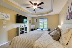 Ein Schlafzimmer mit Bett, Deckenventilator, Fernseher und Fenster mit Jalousien.