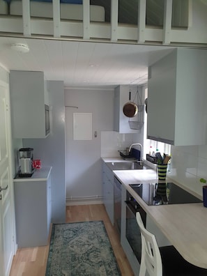 A compact kitchen with white cabinets, a built-in oven, a sink, and a stove. - Cottage above Falu Gruva with wood burning sauna (Slätta-Korsarvet)