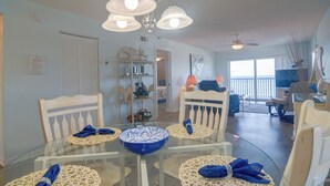 A dining area with a glass table, white chairs, and blue napkins. - Unit w/ Stunning Gulf Views! Steps to Pool & Beach (Madeira Beach)
