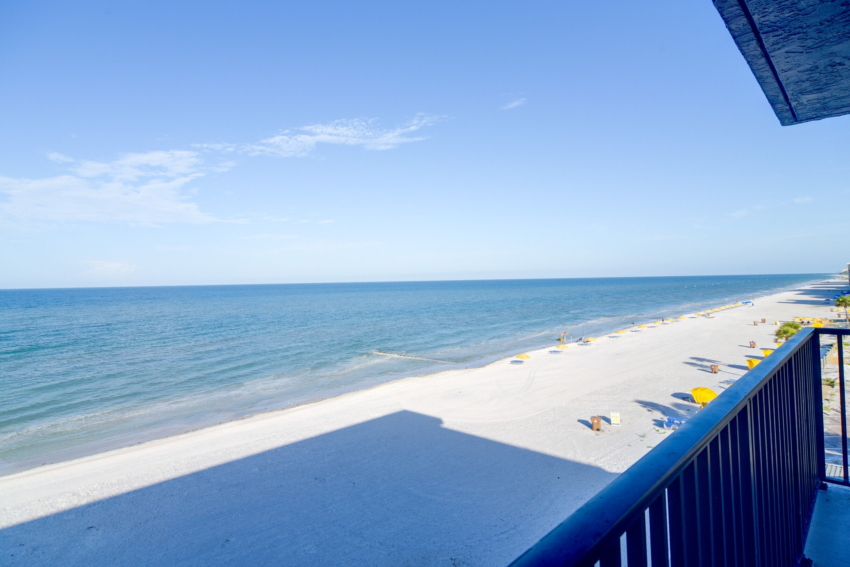 Une plage offrant une vue dégagée sur l’océan, un rivage sablonneux et un balcon doté d’une balustrade.