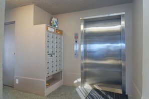 Un ascensor con detalles metálicos, un buzón empotrado en la pared y una pequeña estatua en la parte superior.