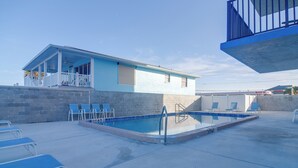 A pool area with a small building, lounge chairs, and a concrete deck. - Unit w/ Stunning Gulf Views! Steps to Pool & Beach (Madeira Beach)
