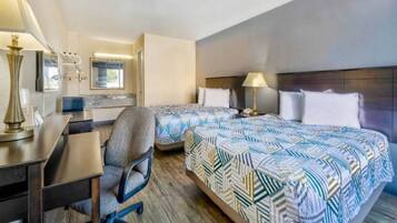 A hotel room with two beds, a desk, a chair, and a lamp.