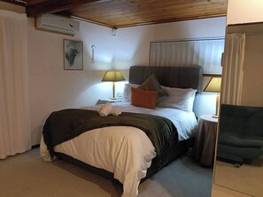A hotel room with a bed, two bedside lamps, a nightstand, a chair, and a window with curtains.