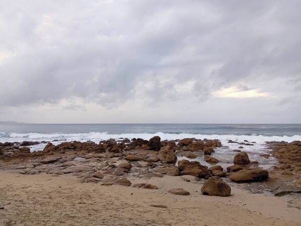 A rocky beach with waves crashing onto the shore under a cloudy sky.