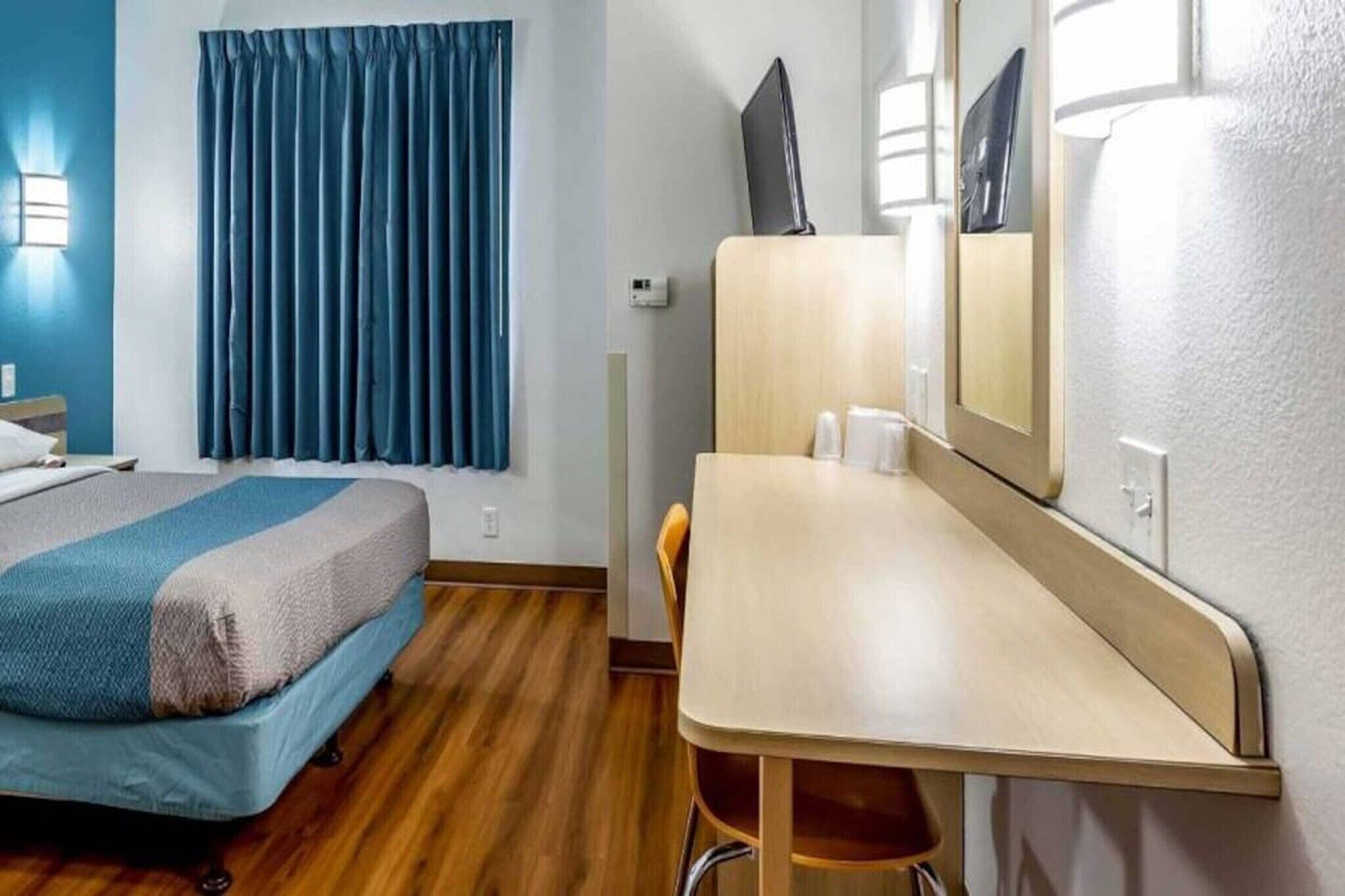 Et hotelværelse med seng, skrivebord, stol, spejl og et vindue med gardiner.