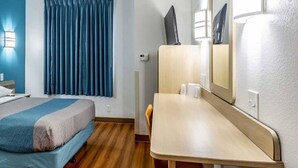 Una camera d'albergo con un letto, una scrivania, una sedia, uno specchio e una finestra con tende.