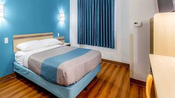 A hotel room with a bed, a window with curtains, a wooden floor, and a chair.