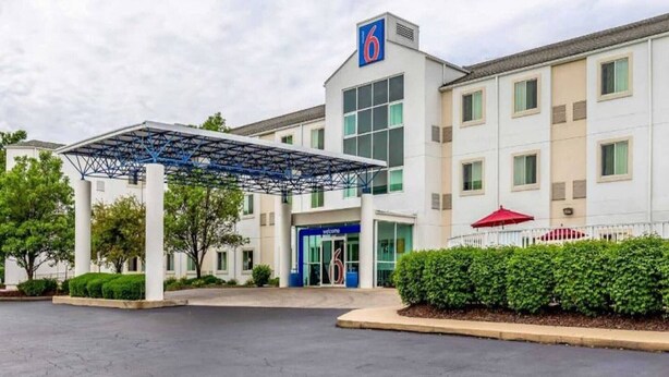 Un hotel con ingresso coperto, un grande insegna con il numero '6' e un ombrello rosso.