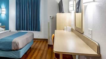 A hotel room with a bed, a desk, a chair, a mirror, and a window with curtains.
