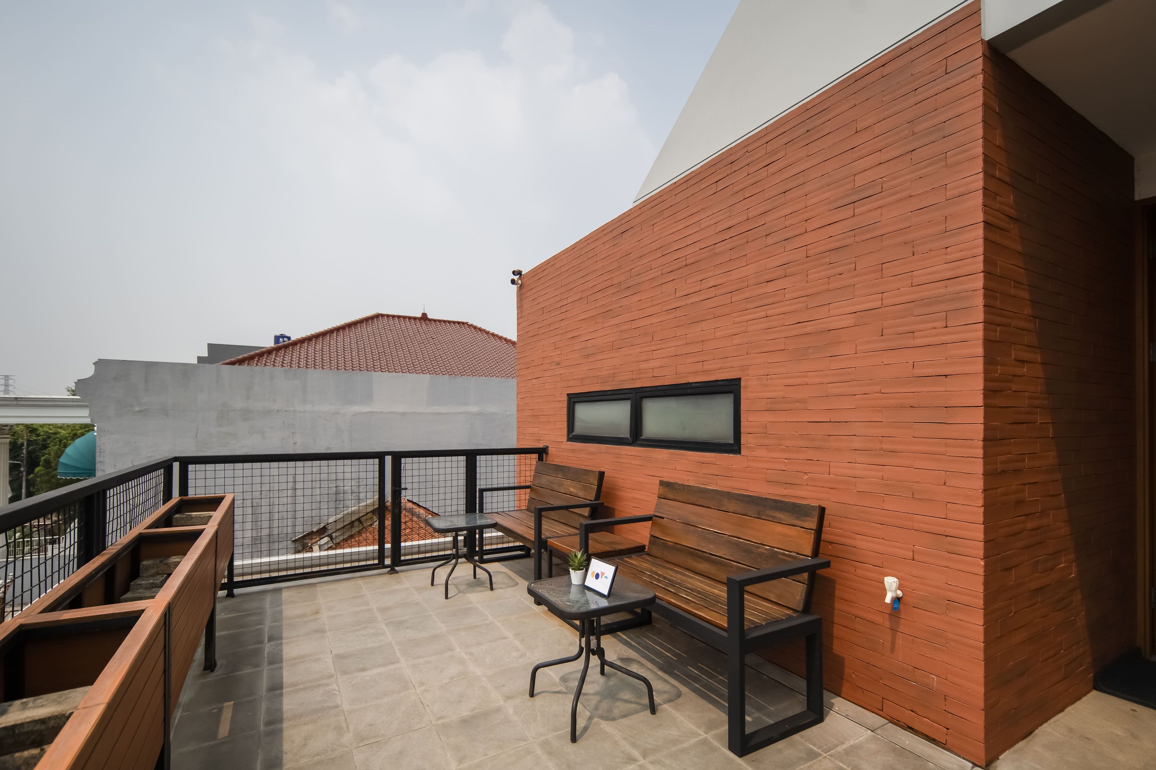 A balcony with a wooden bench and a small table, a tiled floor, and a brick wall.