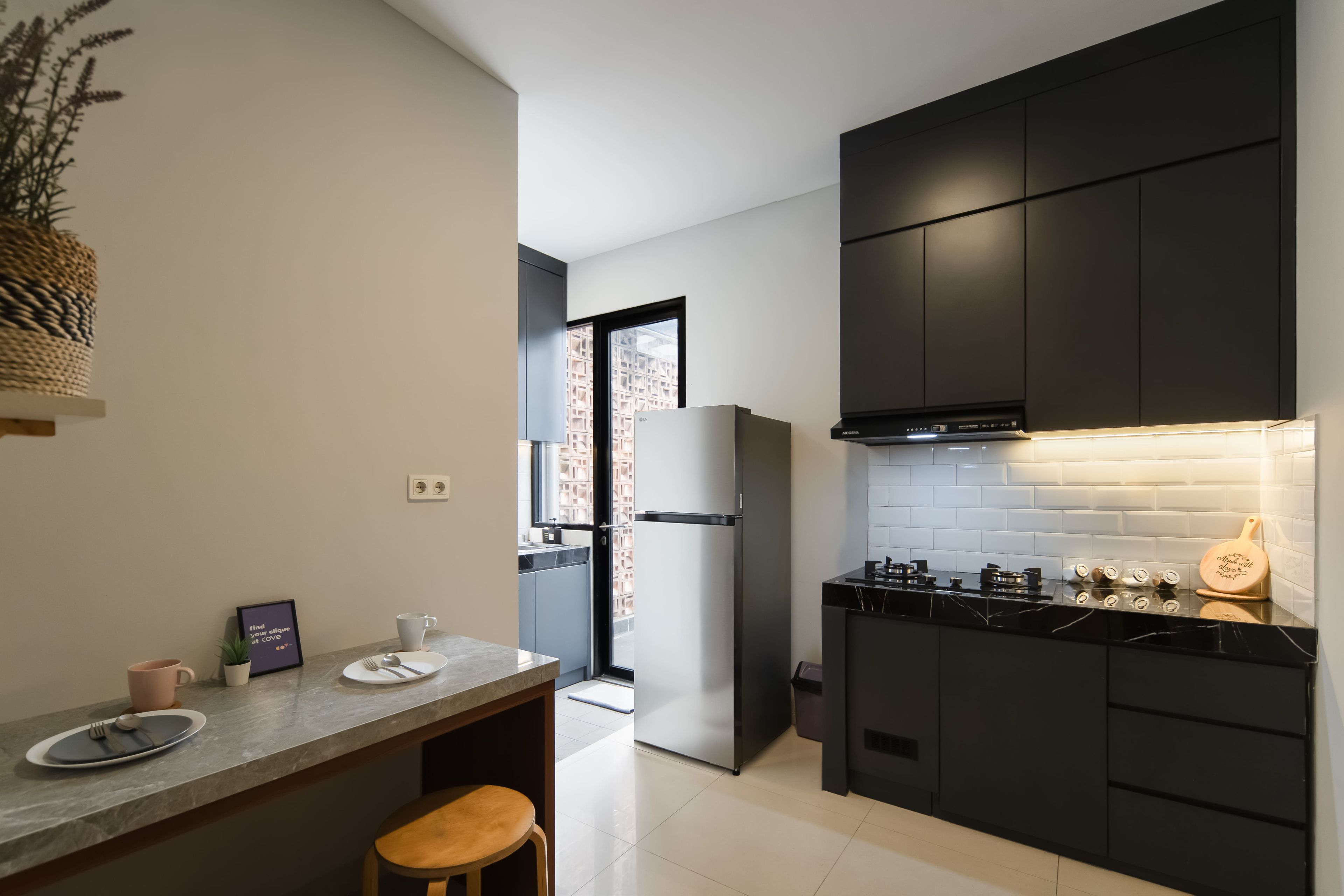 A modern kitchen with dark cabinetry, a stainless steel refrigerator, and a black countertop.