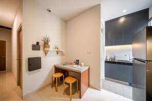 Cocina compacta con estufa integrada, una pequeña zona de comedor con taburetes y un estante en la pared con objetos decorativos.