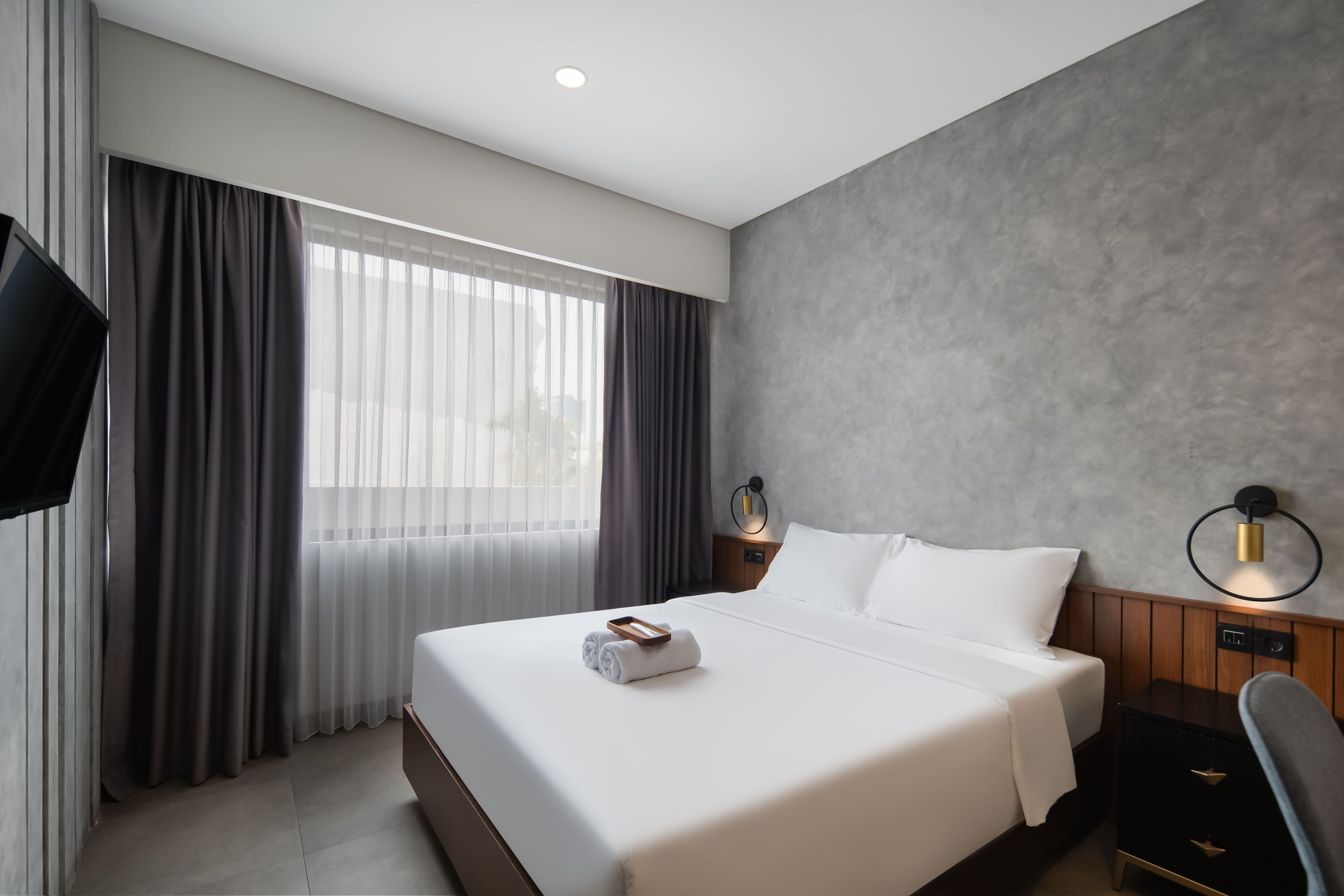 Una habitación de hotel con una cama grande, televisor de pantalla plana, mesita de noche y lámpara de pared.