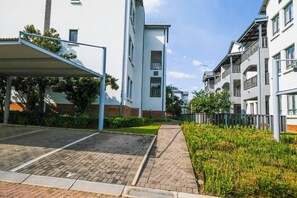 Um edifício residencial com área de estacionamento coberta, um caminho central e um jardim bem cuidado.
