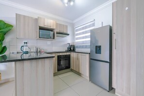 A modern kitchen with light wood cabinets, a built-in microwave, a stove, and a stainless steel refrigerator. - Modern, Peaceful Stay in Broadacres (Chartwell)