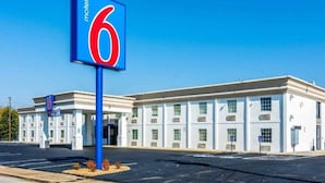 A motel with a prominent '6' sign, a parking lot, and a building facade with multiple windows.