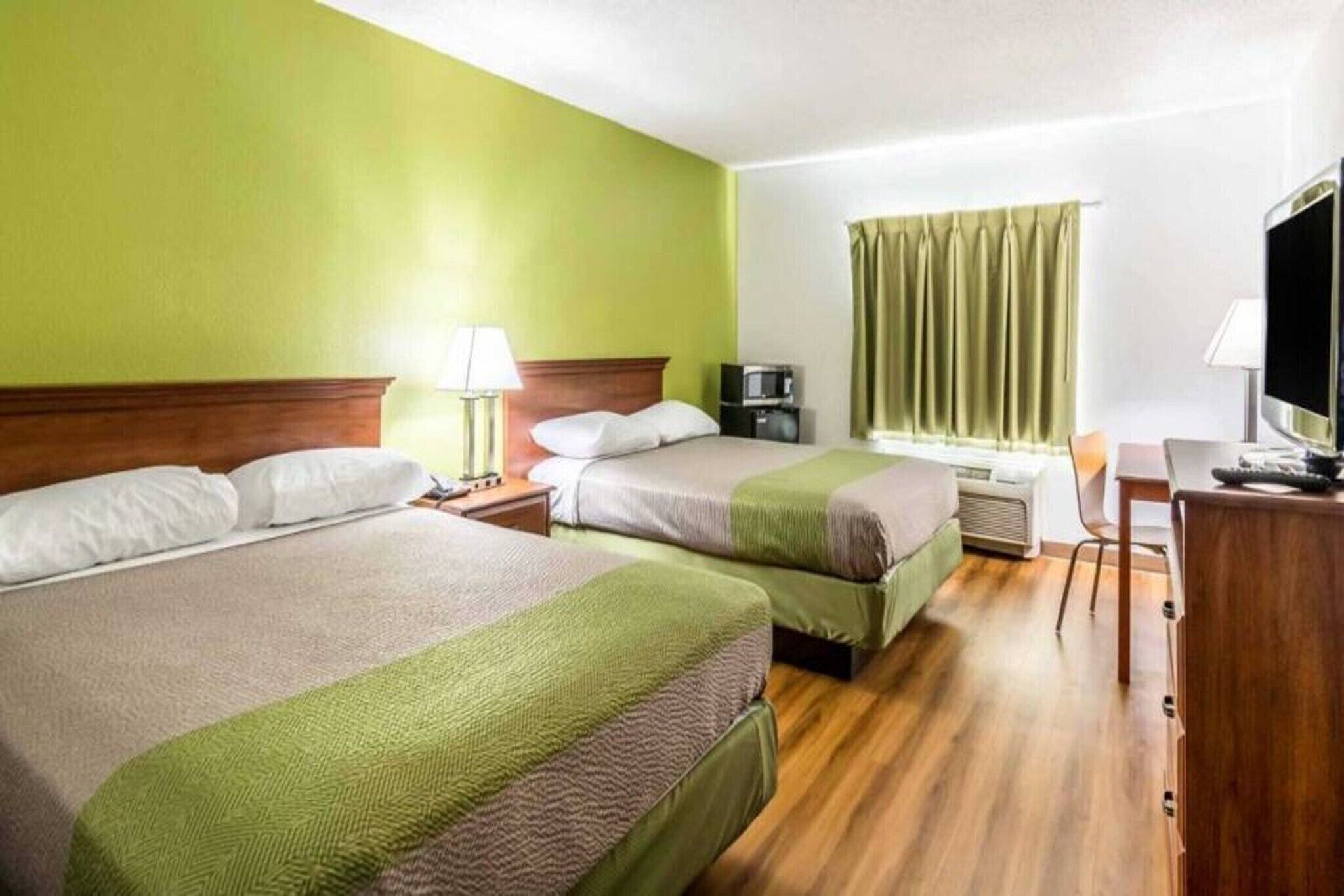 A hotel room with two beds, a desk, a chair, a television, and a window with curtains.