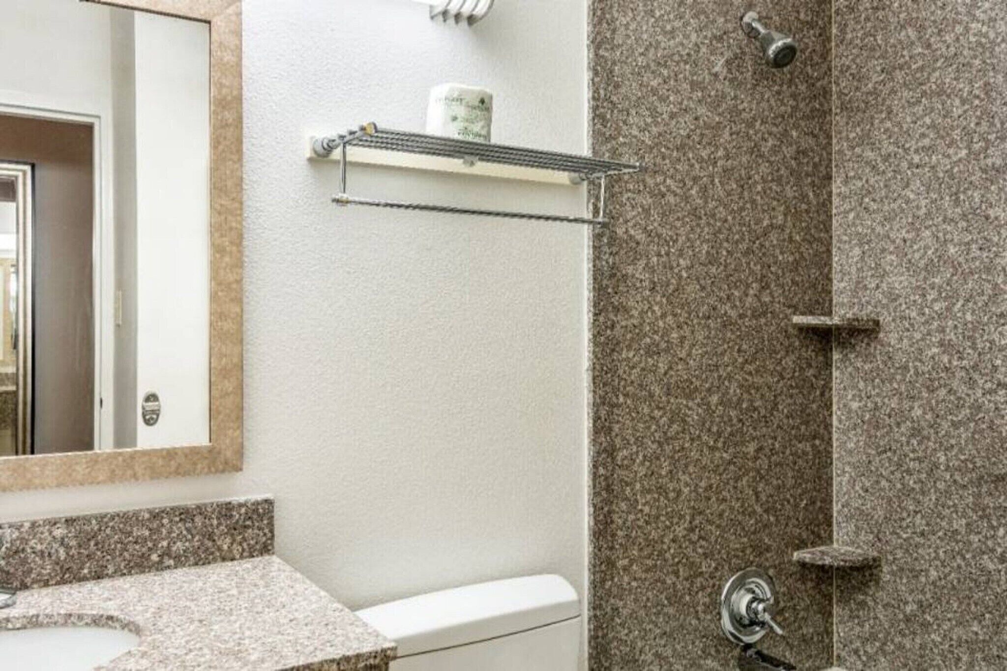 A bathroom with a granite countertop, a mirror, a towel rack, and a shower area with a granite wall.