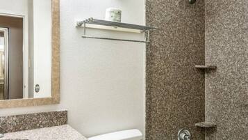 A bathroom with a granite countertop, a mirror, a towel rack, and a shower area with a granite wall.