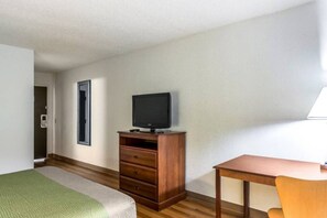 A hotel room with a bed, a wooden dresser, a television, a desk, and a chair.