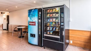 A vending machine with snacks and a water dispenser in a public area with a tiled floor and a bench.
