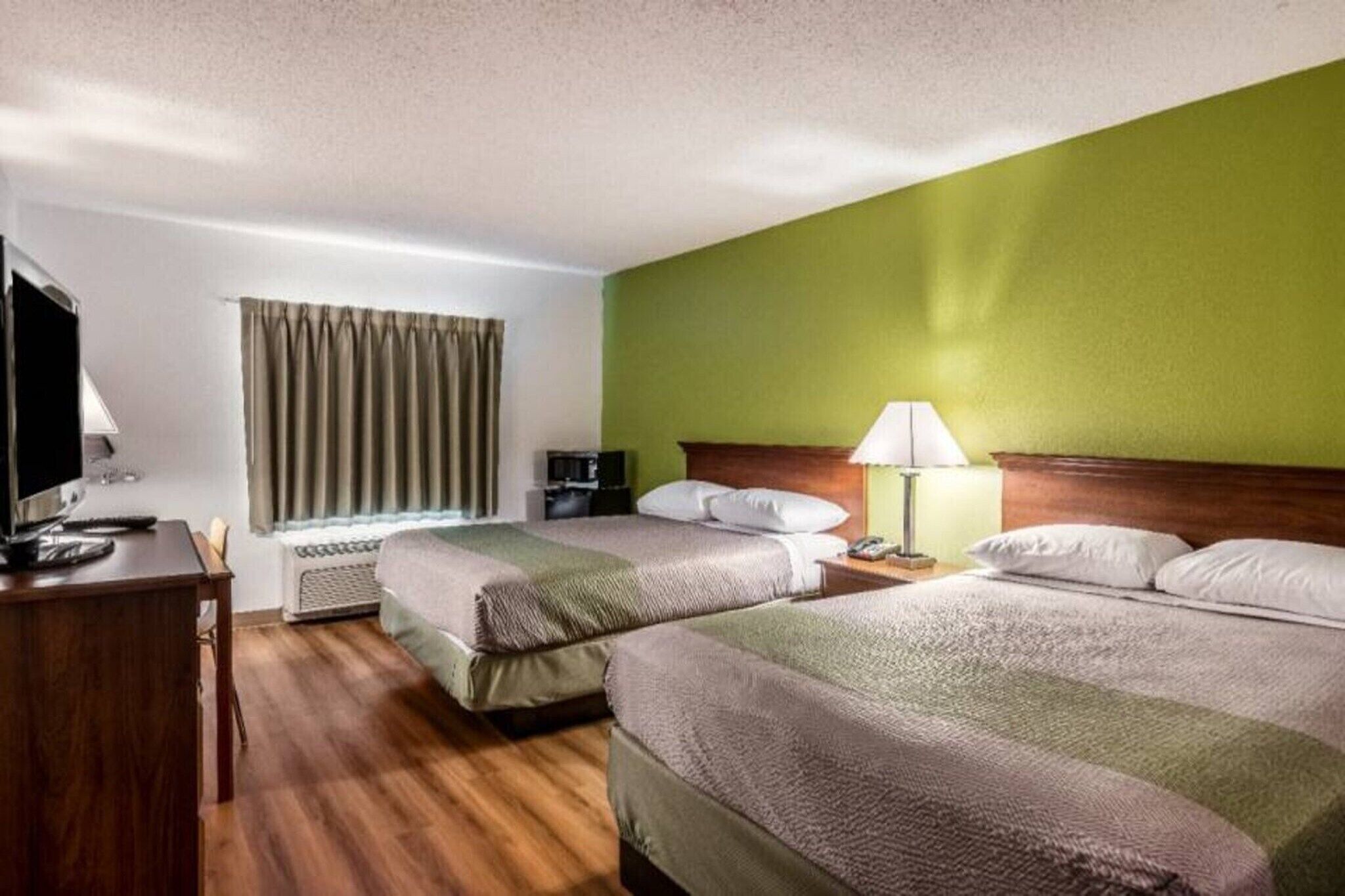 Quarto de hotel com duas camas, uma escrivaninha, uma cadeira, uma televisão e um abajur.