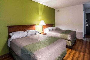 A hotel room with two beds, a nightstand with a lamp, and a wooden floor.