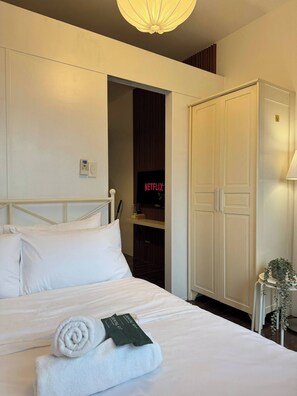 A hotel room with a bed, a wardrobe, a television displaying the Netflix logo, and a bedside table with a lamp and a plant. - Central Makati City View with Fast WiFi and Netflix (Makati City)
