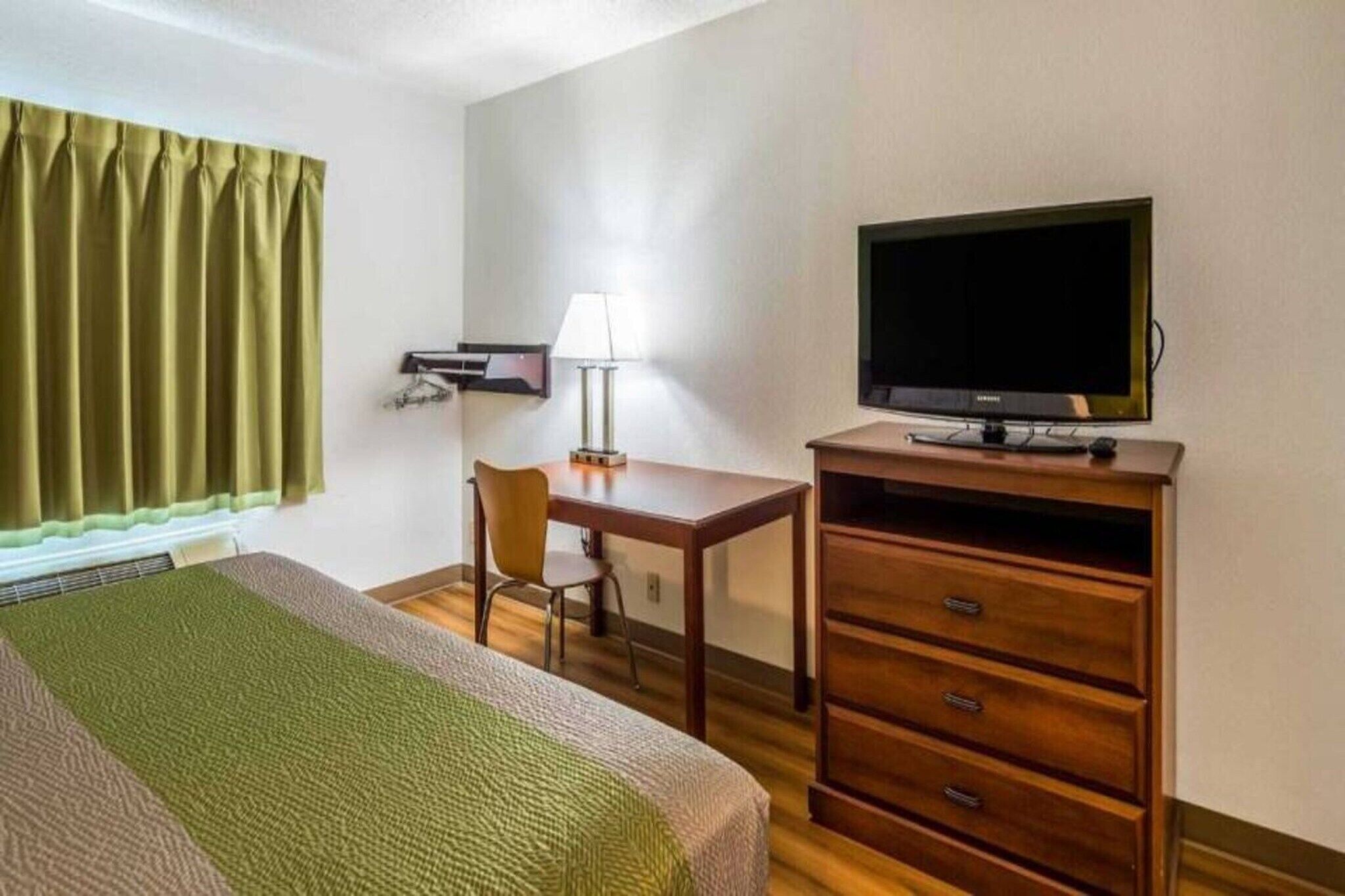 A hotel room with a bed, a desk, a television, and a dresser.