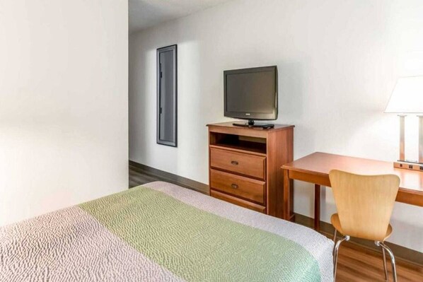 A hotel room with a bed, a desk with a chair, a television, and a wardrobe.