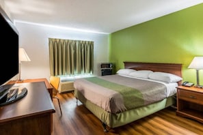 Una habitación de hotel con cama, mesita de noche, lámpara y televisor.