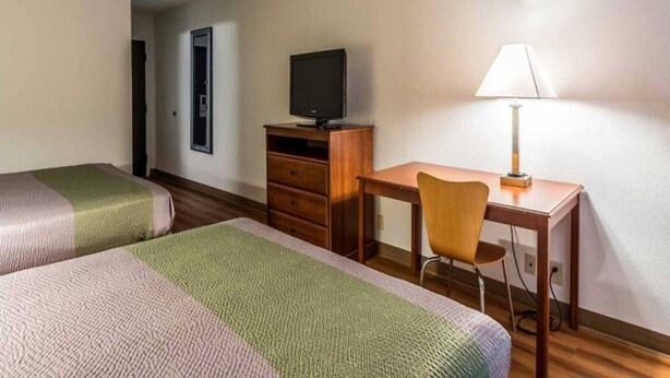 Habitación de hotel con dos camas, un escritorio, una silla, un televisor y una lámpara.