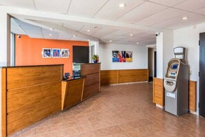 A reception area with a wooden reception desk, a wall-mounted ATM, and a bulletin board with various notices.