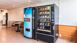 Máquina expendedora con refrigerios y dispensador de agua en un espacio público con piso de baldosas y un banco.