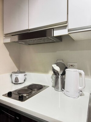 Une cuisine dotée d’un plan de travail blanc, d’une bouilloire électrique blanche, d’une mijoteuse blanche et d’une plaque de cuisson à induction en acier inoxydable.