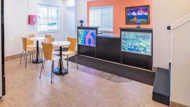 Zona de recepció d'hotel amb un mostrador, una pantalla de televisió i una zona d'estar amb cadires i taules.