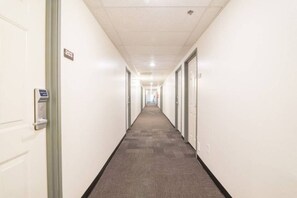 Ein langer, schmaler Hotelgang mit Türen auf beiden Seiten, Teppichboden und einer Decke mit eingelassenen Leuchten.