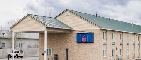 A motel with a large parking lot, a covered parking area, and a sign indicating the number 6.