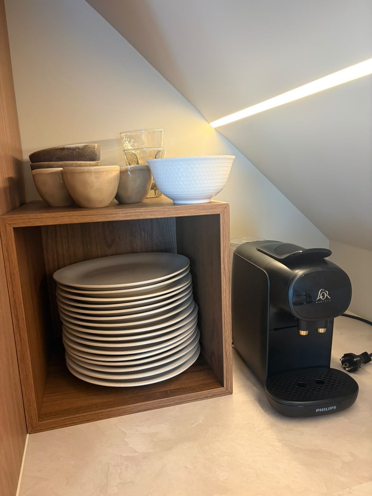 A coffee maker and stacked plates in a wooden cabinet.