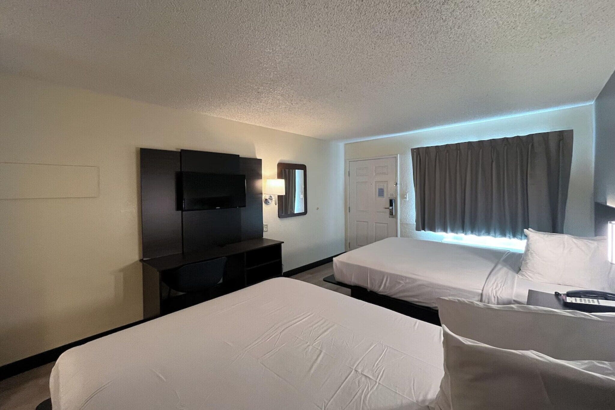 Habitación de hotel con dos camas, televisión, escritorio y ventana con cortinas.