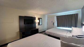 Habitación de hotel con dos camas, televisión, escritorio y ventana con cortinas.